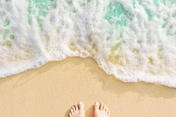 Blue wave and human feet on the sandy beach background