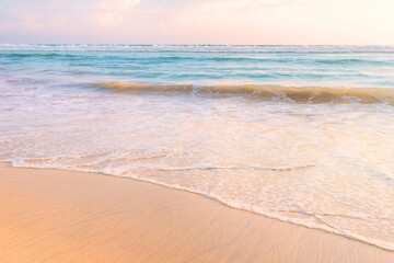 Fototapeta na wymiar Tropical shore. Sandy beach and wavy sea in soft warm sunset light.