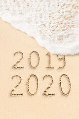 2020 and 2019 handwritten on the sand. New Year concept photo.