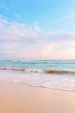 Sandy beach pastel background. Blue cloudy sky and soft ocean wave in warm sunset light