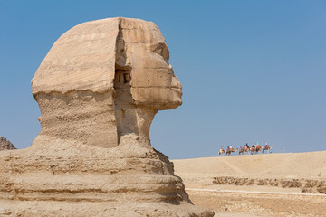 Profile Shot Of The Egyptian Sphinx With People Riding Camels In The Background