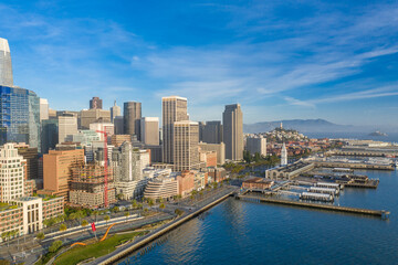 Aerial daytime view of the San Francisco skyline, near the Embarcadero area. Ferry building is visible in foreground, plenty of copy space in blue sky