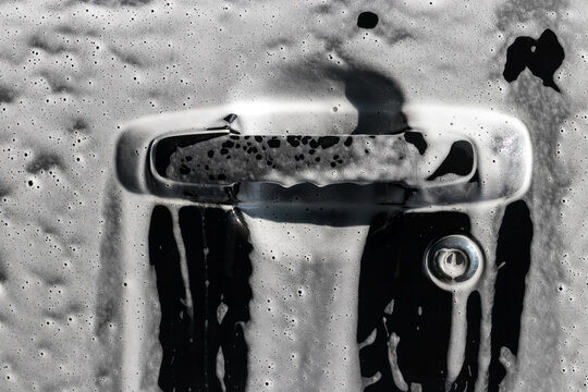 Car washing process: soapy wet surface - black car door handle