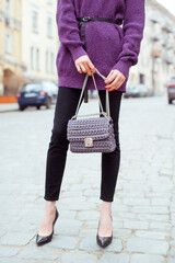 Fashion woman wearing violet knit sweater and holding  gray handbag in hand . Street style .