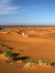 Woman in amazing silk wedding dress with fantastic view of Sahara desert sand dunes in sunset light. Landscape of Morocco, Africa.