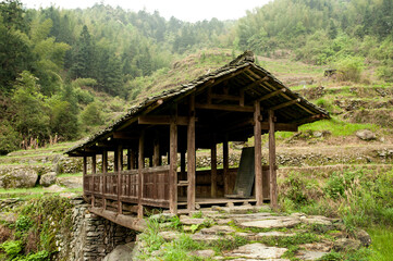 Covered wooden bridge spans stream connecting green rice terraces in Longji, China. 
