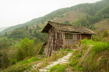 Fototapeta na wymiar Old wooden structure situated on side of green forested hill in Longji, China. Over 100 years old.