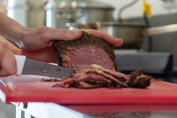 hand cutting slices of pastrami on cutting board making a recipe