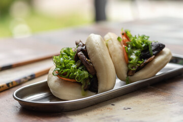 two asian bao stuffed with lettuce vegetables and pork belly on a wooden table and chopsticks