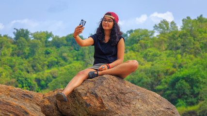 Portrait smiling young asian girl sitting on a rock, posing for a selfie