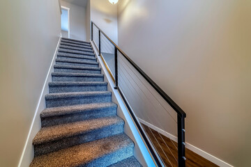 Indoor stairs of home with metal handrail and gray carpet on the treads