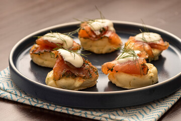 dried smoked salmon gravlax with dill and sour cream on blini pancake and blue ceramic plate and napkin on wooden table
