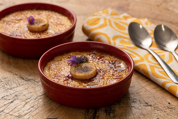 cream creme brulee with banana on ceramic dessert bowl on napkin and spoons