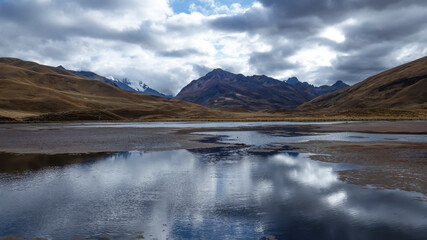 Landscape photo of a lake in the Peruvian Andes with impressive mountains, dynamic light conditions and water reflections of the cloudy sky, Huascarán National Park