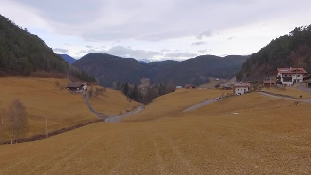 Aerial: Drone flying forward towards car on road in village near mountains against sky - Dolomites, Italy