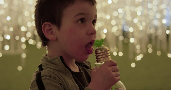 Toddler boy sipping bendy straw surrounded by hundreds of string lights