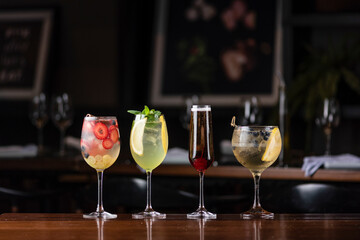 four different colorful drinks on a wooden table at a fancy restaurant bar with blurred background