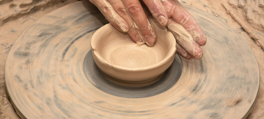 Woman hands in clay at process of making clay bowl on pottery wheel