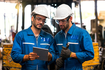 Mechanic holding a wrench and a tablet standing in front of an industrial forklift