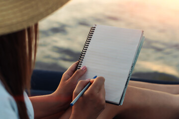 Young woman in straw hat writing in a notebook at nature. Inspiration concept