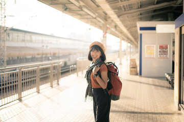 Young Asian woman traveller with backpack waiting for train at train station. A woman happy with...