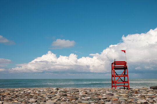 Red lifeguard rescue tower on the empty rocky beach with blue cloudy sky background