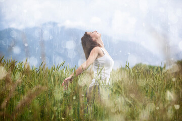 Joyful blonde girl enjoys her evening in the countryside by dancing in the rain - 357539107