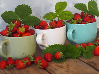 Summer berry theme.Strawberry in three porcelain cups on a wooden table. Copy space.