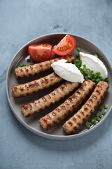 Grey plate with grilled serbian cevapi or cevapcici and kajmak cheese, vertical shot on a grey concrete background