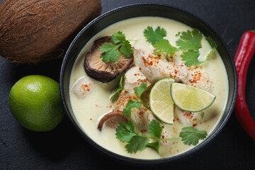 Black bowl of tom kha or thai traditional coconut milk and chicken soup, studio shot, selective focus
