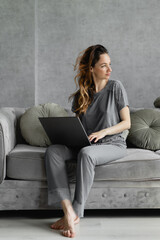 Obraz premium Modern business lady working from home sitting on the couch with a laptop on her lap. Conference with business partners from the apartments. Webcam chat and weekend conferencing.