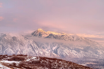 Snowy Wasatch Mountain and hill top towering over Utah Valley under cloudy sky