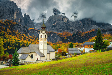 Traditional alpine church and street view with mountains, Dolomites, Colfosco