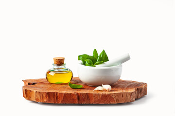 Basil leaves in a mortar, garlic and olive oil on a wooden cutting board. White background. Isolated.