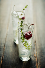 Gin based cocktail with cherries and thyme herbs on the rustic background. Selective focus. Shallow depth of field.