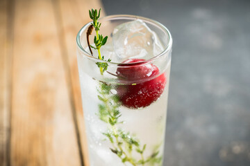 Gin based cocktail with cherries and thyme herbs on the rustic background. Selective focus. Shallow depth of field.