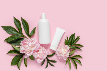 Cosmetic bottle containers with peony flowers on a pink background. Blank label for branding mock-up, Copy space.