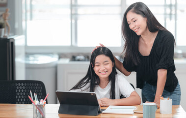 Happy family, young attractive mother and pretty daughter doing homework together at home.