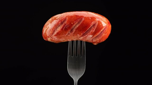 sausages. grilled sausage on black fork rotating. black background