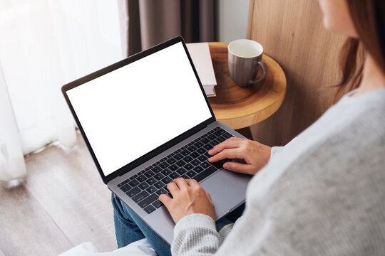 Top view mockup image of a woman working and typing on laptop computer with blank screen while sitting in bed at home