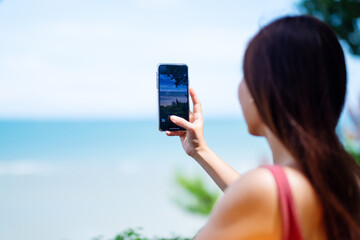 Rear view image of a woman using mobile phone to take a photo of a beautiful beach and sea