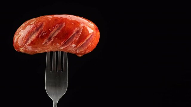 sausages. grilled sausage on black fork rotating. black background