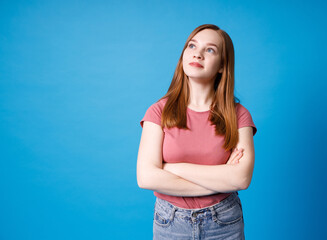 Young ginger girl in pink t-shirt and jeans posing isolated on blue wall background studio portait. Mock up copy space.