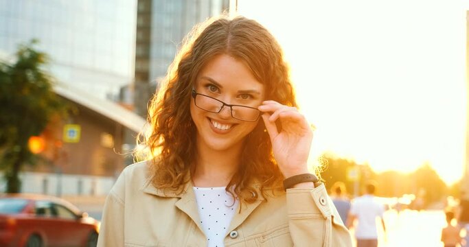 Portrait of girl student on sunset, touching glasses, looks clever and smart.