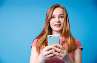 Happy girl with surprised expression looks at the phone. Photo of girl in in a pink t-shirt on blue background.