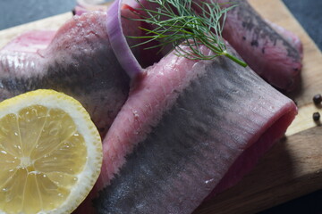 Fillet of Herring fish  on wooden board  with pepper, herbs, red onion and lemon on black  background. Top view with copy space with potatoes 