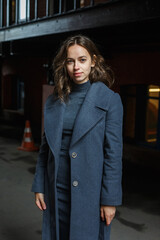 Obraz premium young thoughtful smiling pretty girl in gray coat and turtleneck poses outdoors. Street style portrait photo session of attractive female, urban photoshoot of beautiful elegant model