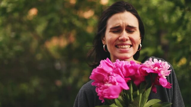 Woman listening greeting or compliment and take a flower. Celebration and presents. Young woman in grey hoody holding bouquet of beautiful pink peonies flowers.