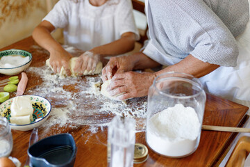 Obraz na płótnie Canvas Cropped image of the hands of an old woman and a child kneading dough, top view of the dough. Ingredients and utensils for baking arranged on a wooden table.