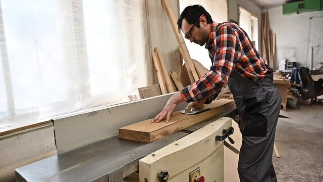 Working process in the carpentry workshop.A man in overalls uses sthicknessing planer machine in a carpentry workshop.Profession, carpentry, woodwork and people concept